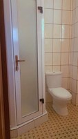 Un baño con inodoro, cabina de ducha y paredes con azulejos.