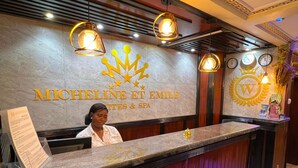 A reception desk with a marble top, a woman seated behind it, and a logo above. - Résidences hôtelières Micheline et Emile, Bastos (Yaoundé)