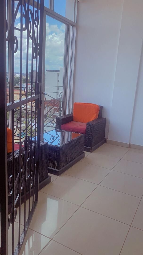 A balcony with wicker furniture, a glass table, and a metal gate.