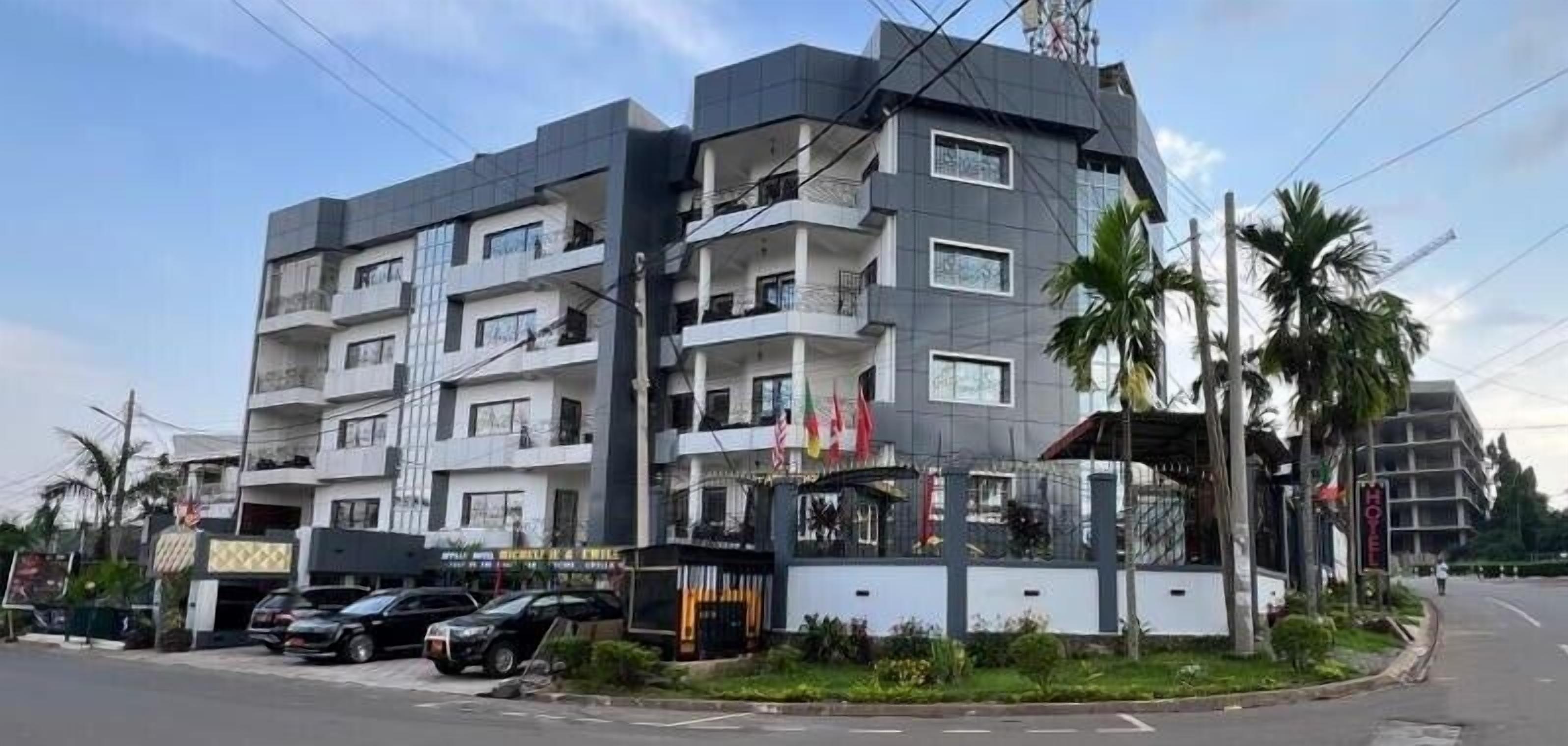 A multi-story building with balconies, a parking area, and a small garden.