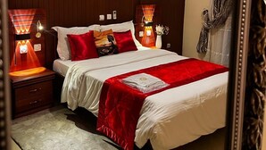 A hotel room with a large bed, two bedside lamps, a wall art piece, and a mirror. - Résidences hôtelières Micheline et Emile, Bastos (Yaoundé)