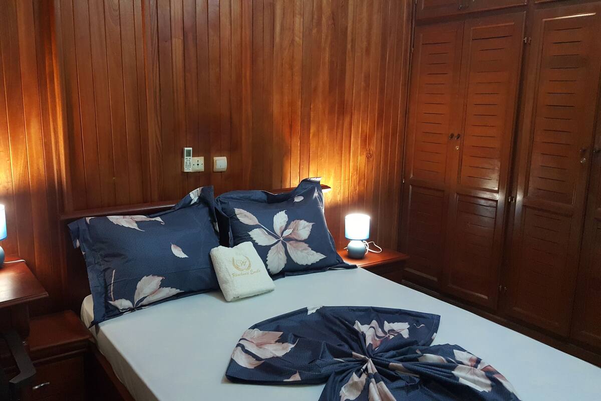 Habitación de hotel con paneles de madera, una cama con ropa de cama floral, lámparas de noche y un armario.