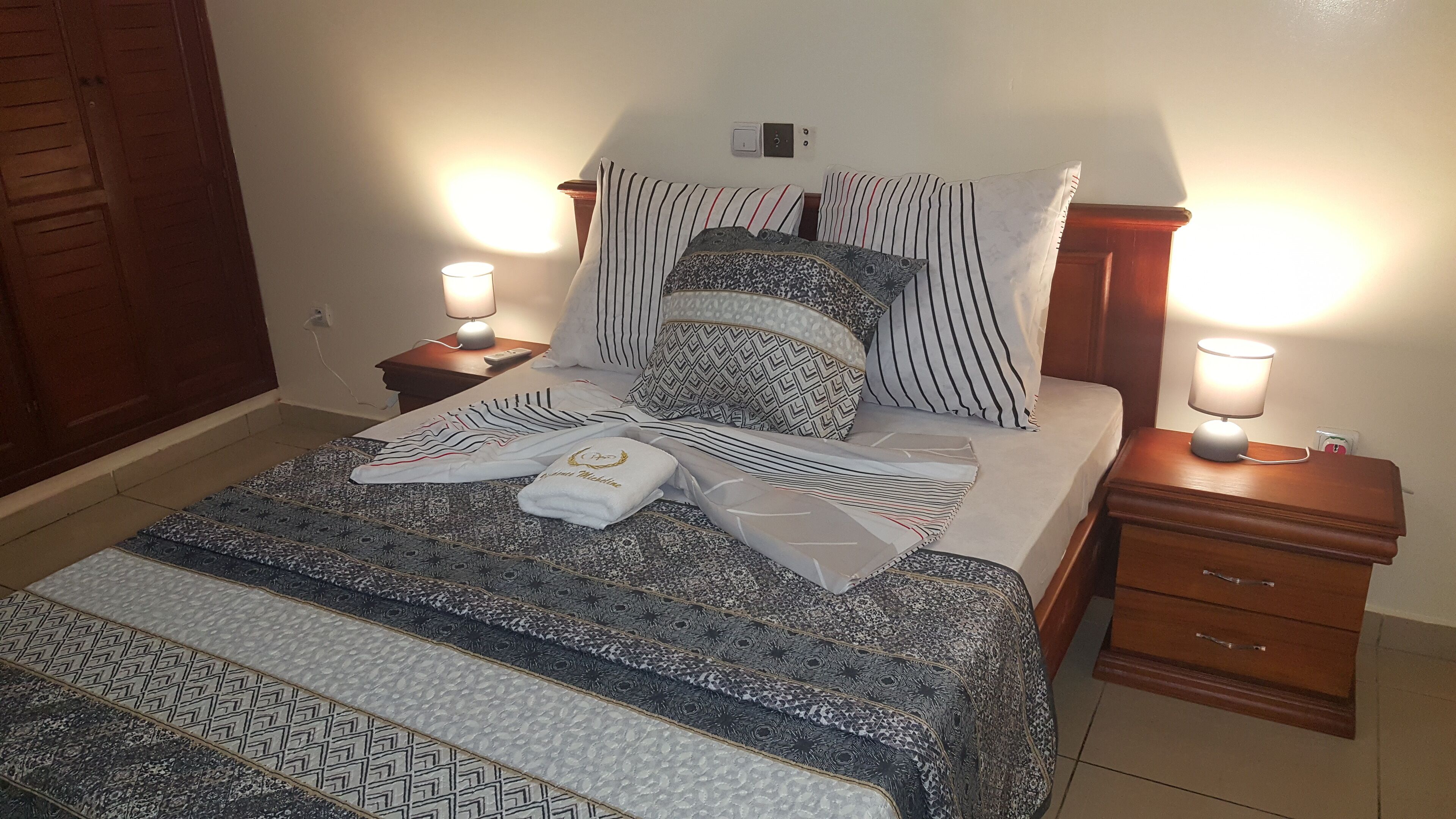 Una cama bien hecha con ropa de cama estampada, dos mesitas de noche con lámparas y una puerta de madera al fondo.