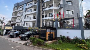 A multi-story hotel with balconies, a gated entrance, and a parking area with cars. - Résidences hôtelières Micheline et Emile, Bastos (Yaoundé)