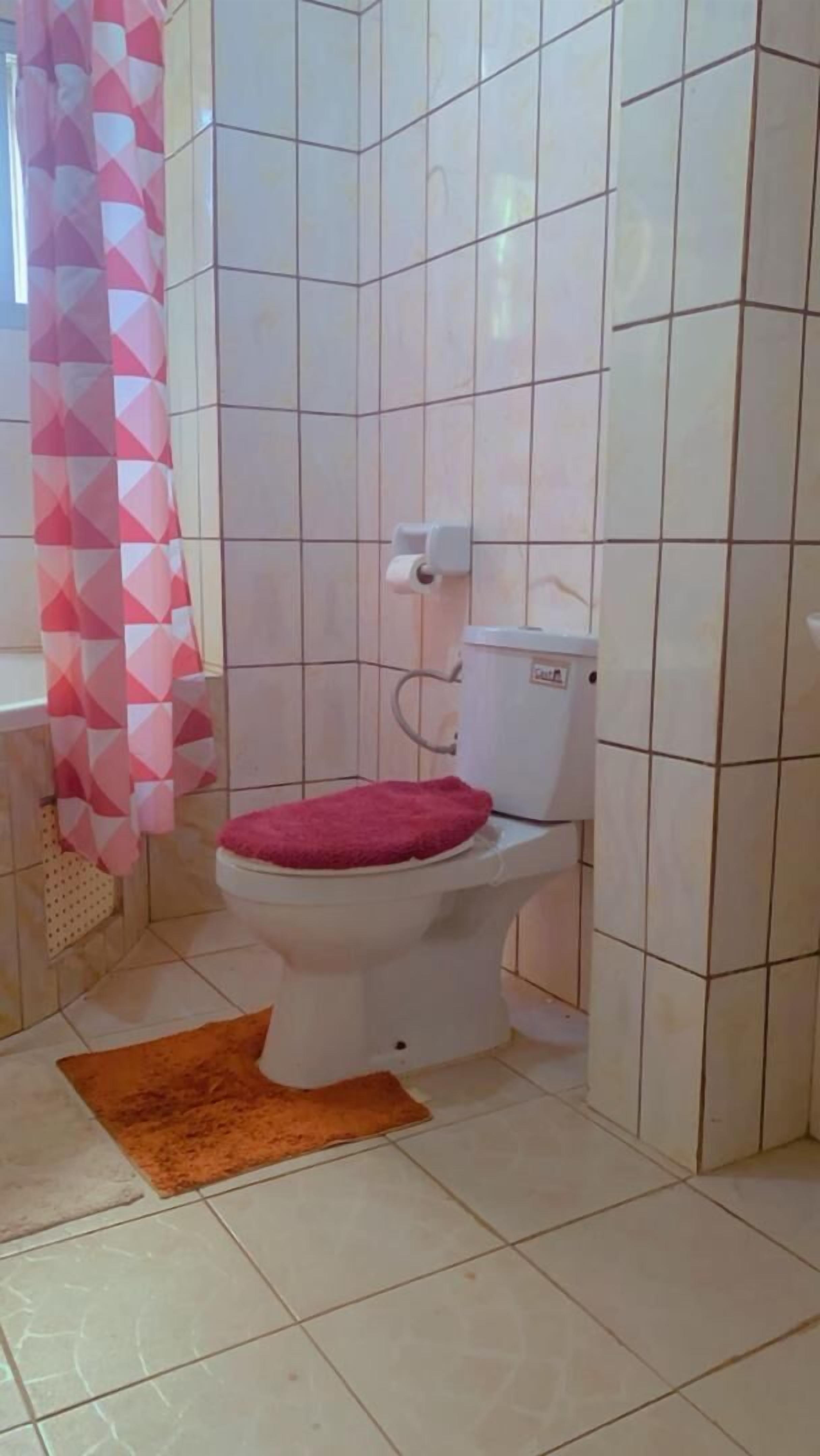 A bathroom with a toilet, a pink patterned shower curtain, and a brown rug.