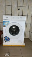 Una lavadora blanca con un panel de control, sobre una plataforma amarilla.