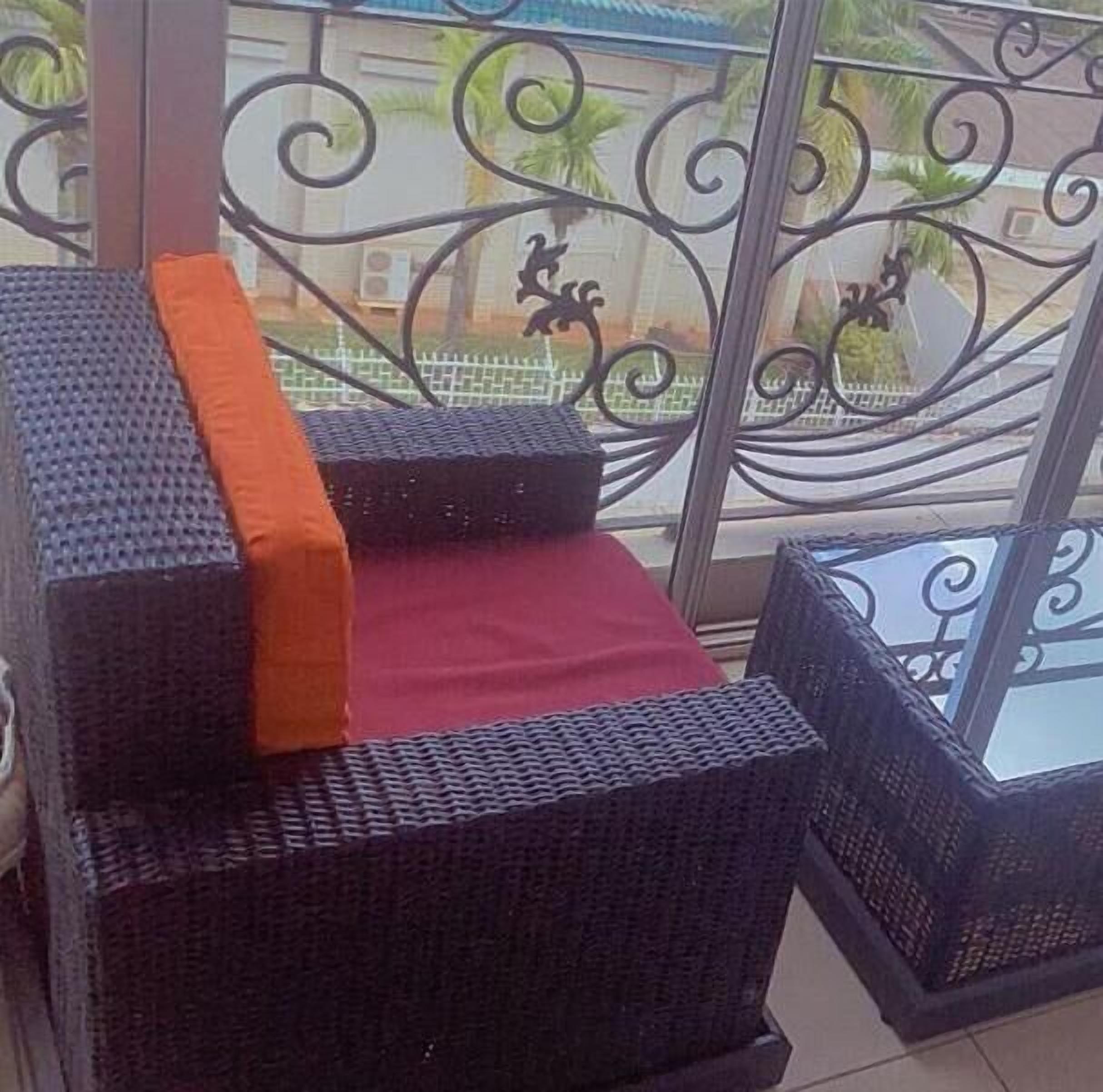 Un balcon agrémenté de meubles en osier, notamment une chaise et une petite table, ainsi que d’une rambarde décorative en métal.