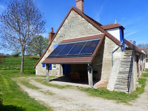 Een stenen huis met een schuin dak, een zonnepaneel op het dak en een trap die naar de bovenverdieping leidt.