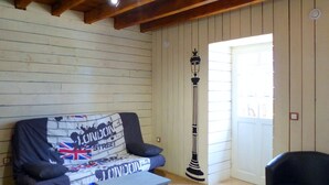 A room with a wooden ceiling, a sofa with a London Street-themed cover, a tall black lamp, and a door leading outside. - Renovated eco-lodge with wifi near Vichy (Bransat)