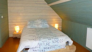A bedroom with a sloped ceiling, wooden walls, and a bed with a white sheet and pillows featuring the word "NATURE" repeatedly. There are two bedside lamps on wooden nightstands. - Renovated eco-lodge with wifi near Vichy (Bransat)