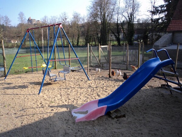 A playground with a swing set and a slide, surrounded by sand and trees.