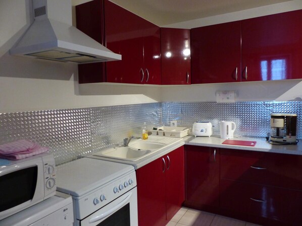 A kitchen with red cabinets, a white stove, a microwave, and a coffee maker.