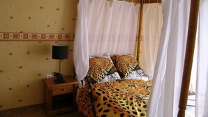 Un lit recouvert d’une couvre-lit à motifs léopard, une table de chevet avec une lampe et un lit à baldaquin.