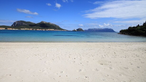 A beach with clear blue water, sandy shore, and distant mountains. - Villetta has two levels with beautiful sea view and located in front of a small park for children an (Golfo Aranci)