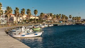 A waterfront marina with boats docked along a wooden pier, surrounded by palm trees and buildings with Mediterranean architecture. - Villetta has two levels with beautiful sea view and located in front of a small park for children an (Golfo Aranci)