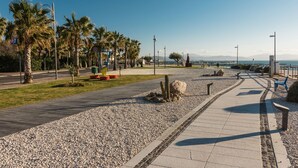 A coastal promenade with palm trees, a pebble path, and benches. - Villetta has two levels with beautiful sea view and located in front of a small park for children an (Golfo Aranci)