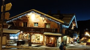 A hotel with a traditional wooden facade, illuminated by string lights and a sign indicating it is a hotel. - Appartement Plein Centre du Chinaillon (Le Grand-Bornand)