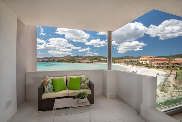 Ein Balkon mit einer Couch und einem Couchtisch, mit Blick auf einen Strand und ein Resort.