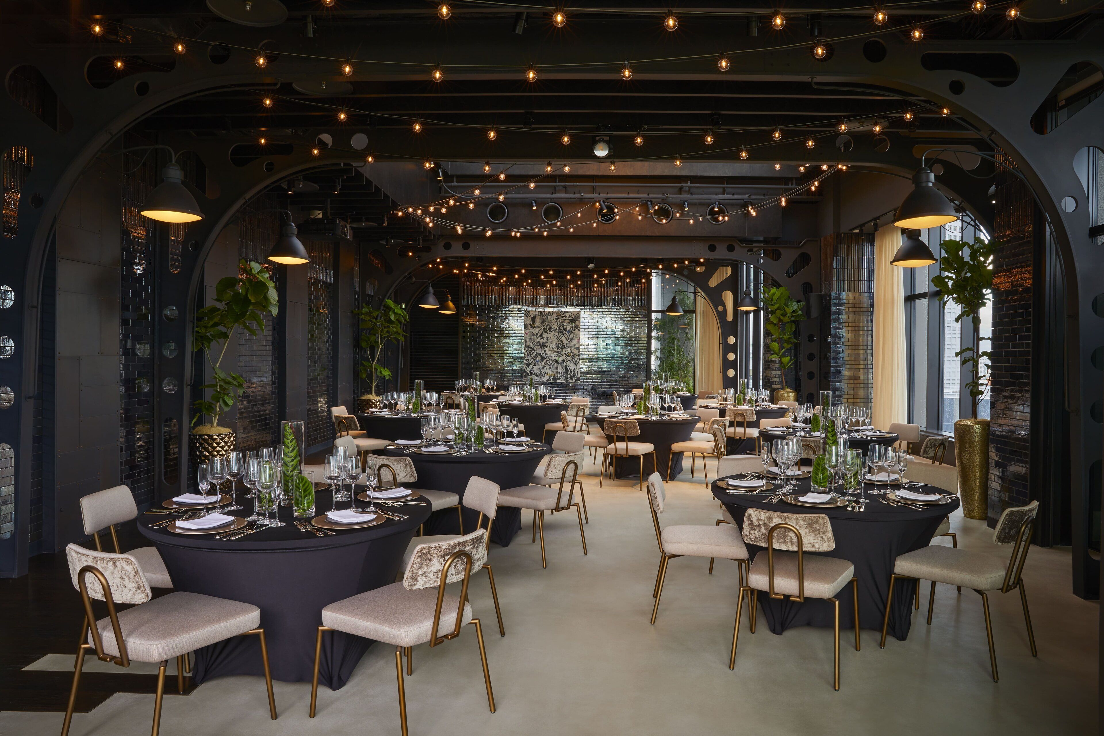 A spacious dining area with round tables, chairs, and string lights.