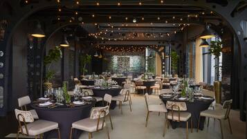 Un vaste espace dédié à la salle à manger, avec des tables rondes, des chaises et des guirlandes lumineuses.