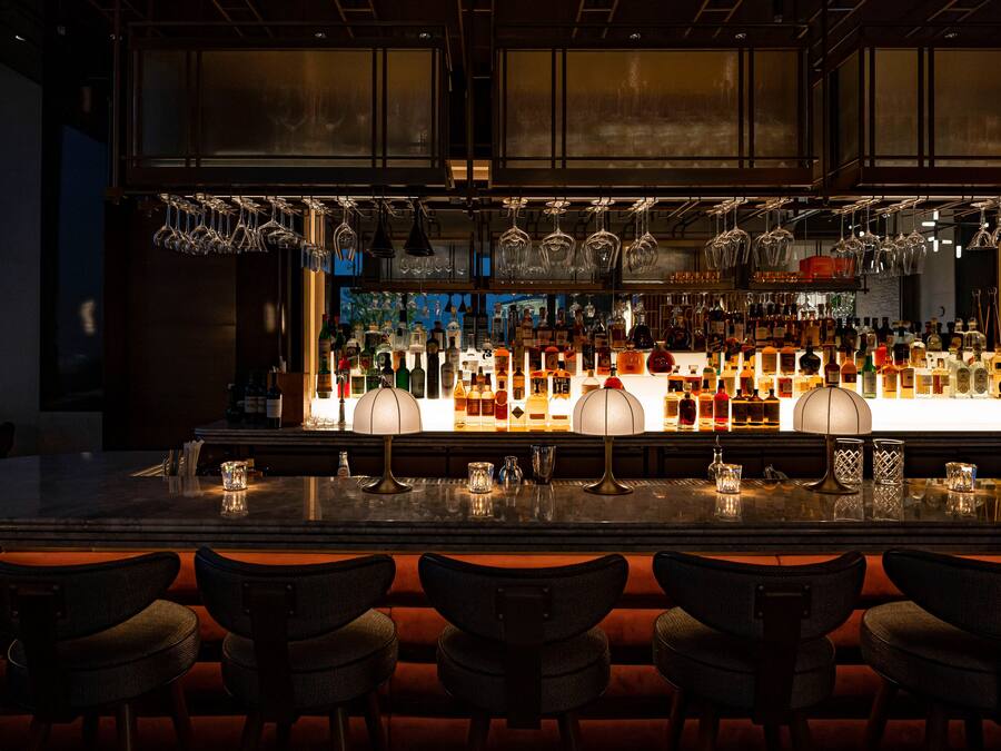 Een bar met verschillende zitmogelijkheden, een goed gevulde bar en hangend glaswerk.