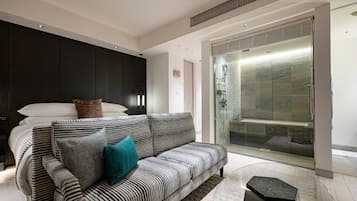 A modern bedroom with a large bed, a striped sofa, and a glass-enclosed shower area.