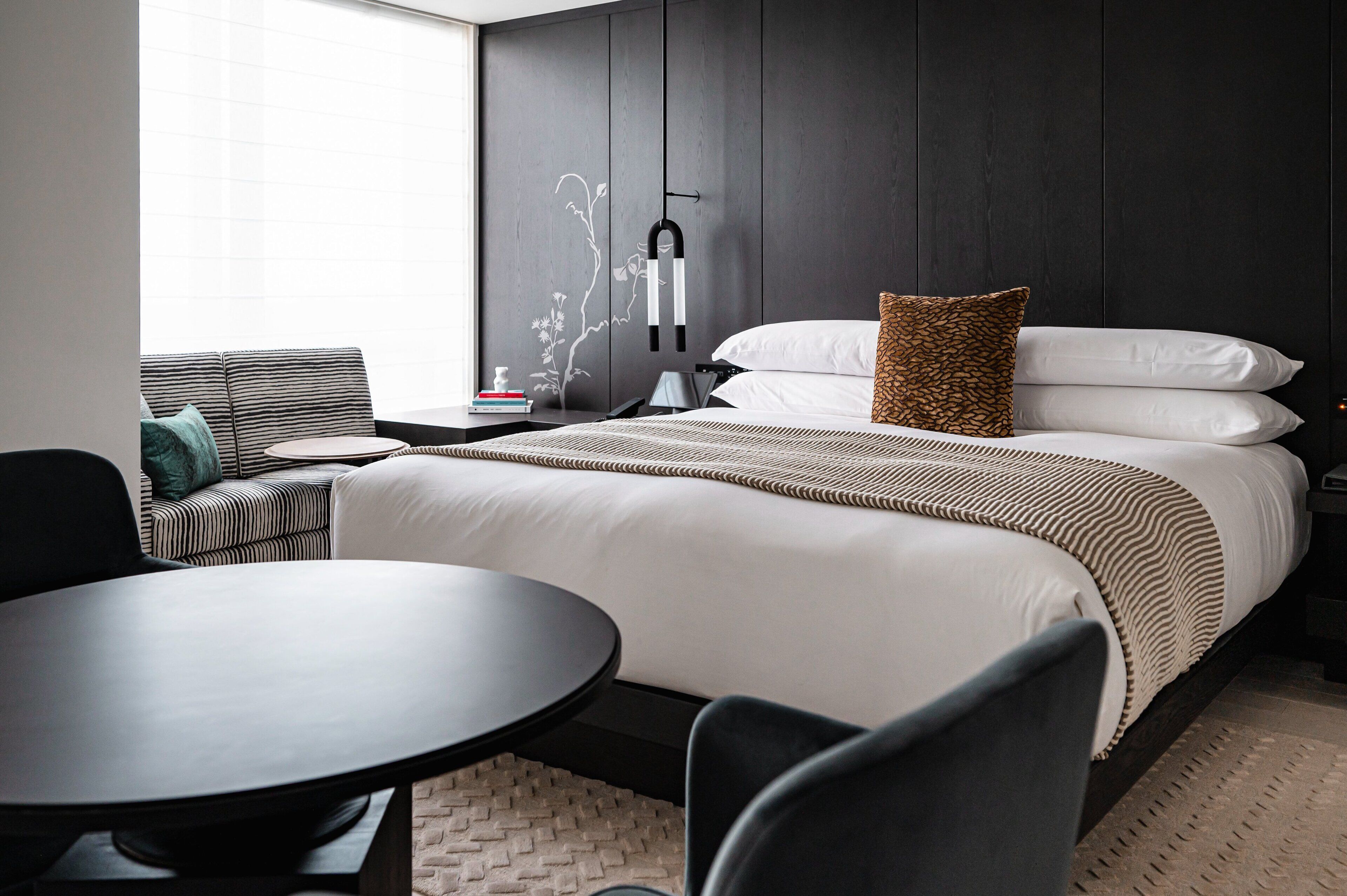 A modern hotel room with a bed, a sofa, a table, and a wall-mounted lamp.