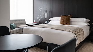 A modern hotel room with a bed, a sofa, a table, and a wall-mounted lamp.