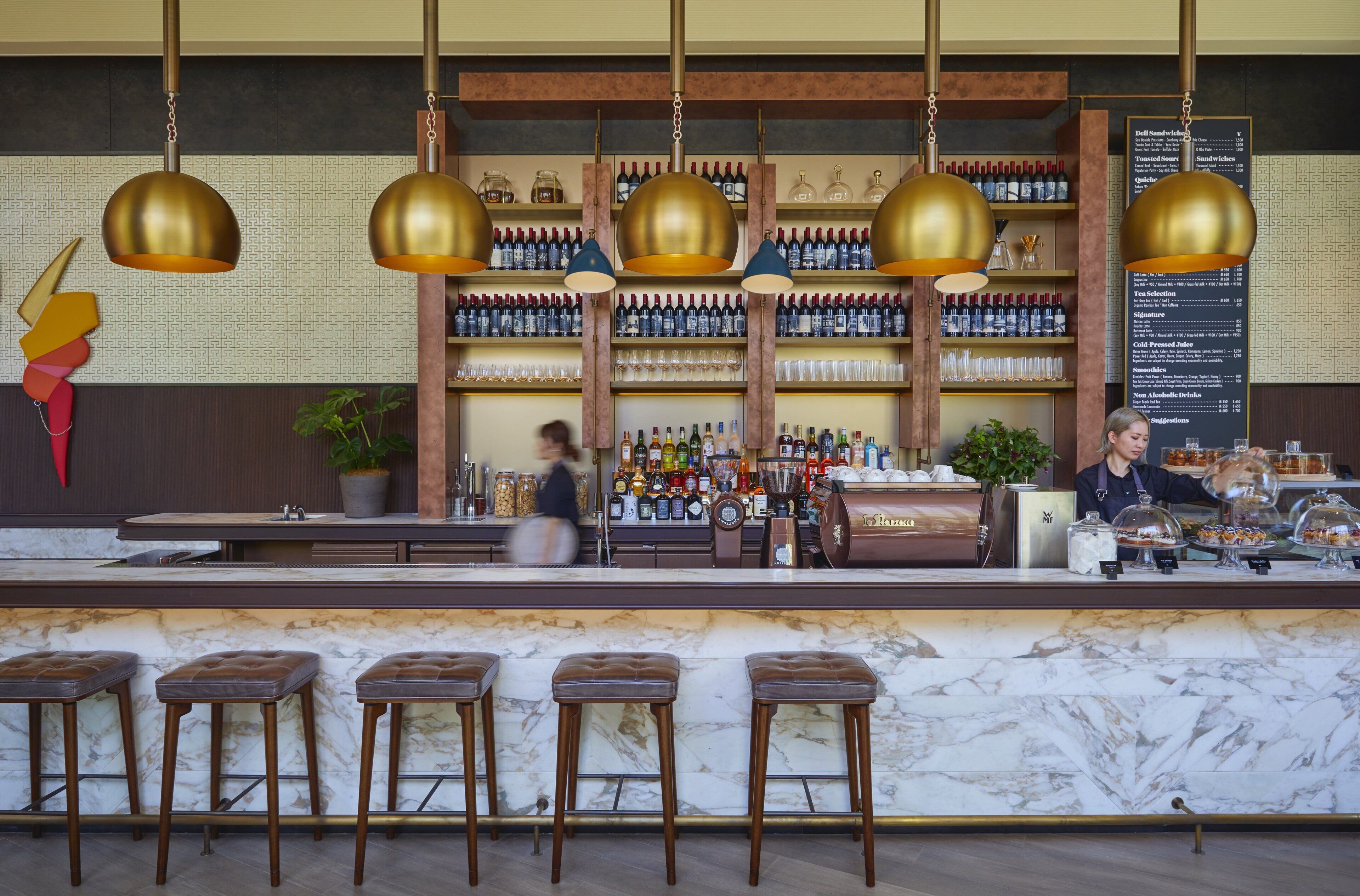 A bar area with marble countertops, multiple stools, and a variety of bottles and glasses on shelves.