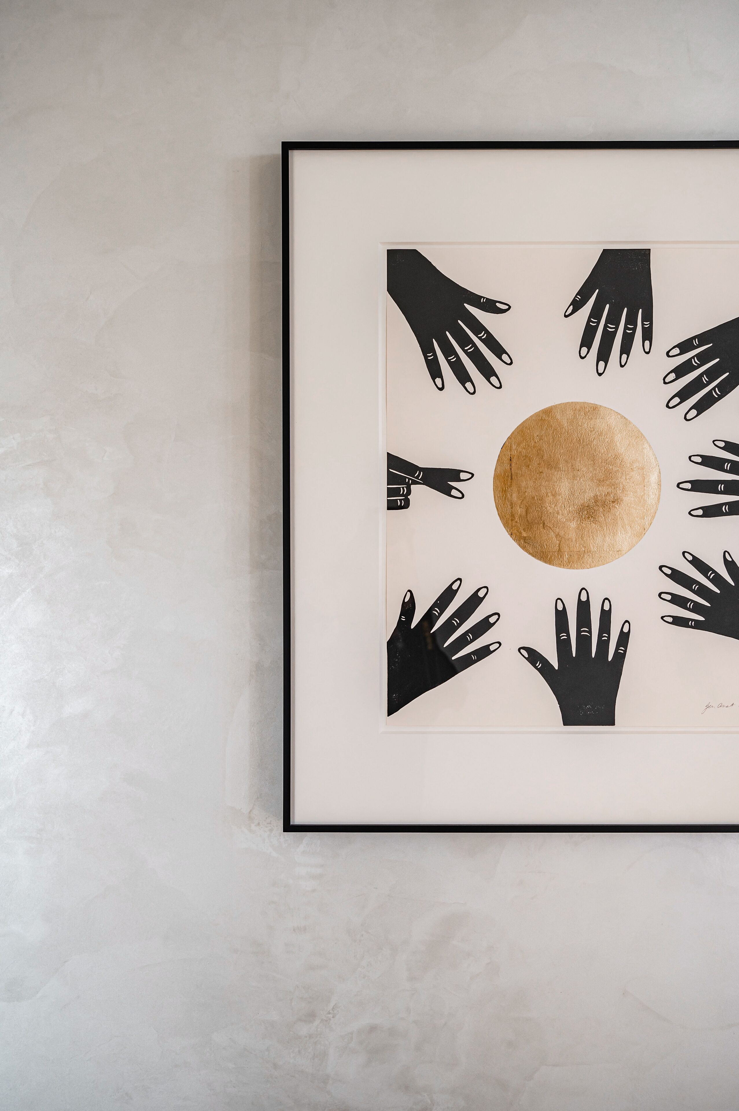 Une œuvre d’art encadrée, composée de plusieurs mains noires disposées autour d’un cercle central de couleur marron.