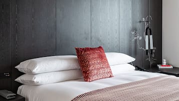 A modern hotel room with a large bed, dark wood paneling on the walls, a red and white striped throw blanket, and a nightstand with a lamp.