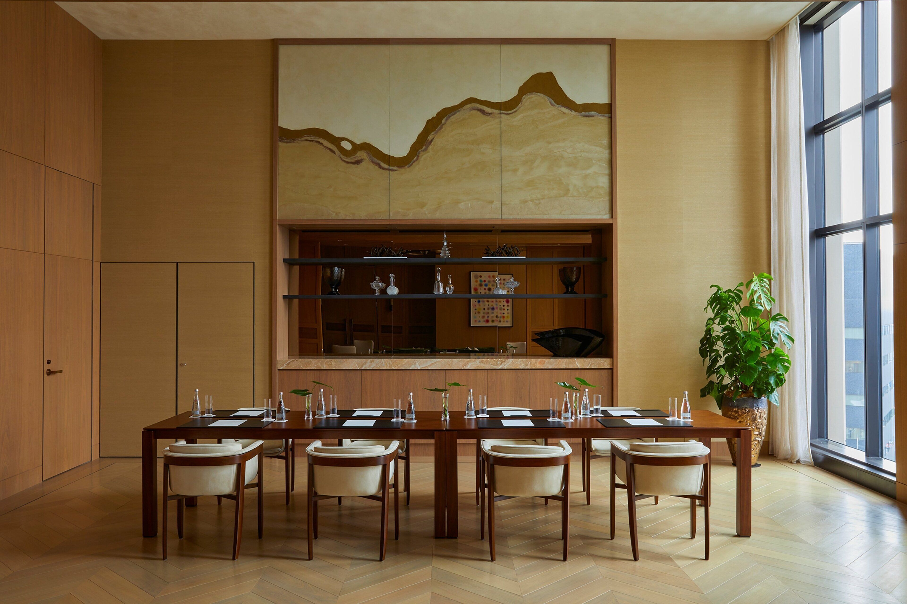 Un comedor con una mesa larga dispuesta para seis personas, bordeada por sillas de madera. Un panel decorativo grande con un diseño de ola se encuentra sobre la mesa.