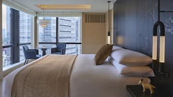 A modern hotel room with a large bed, a view of the city, a small table with a chair, and a decorative dog figurine.
