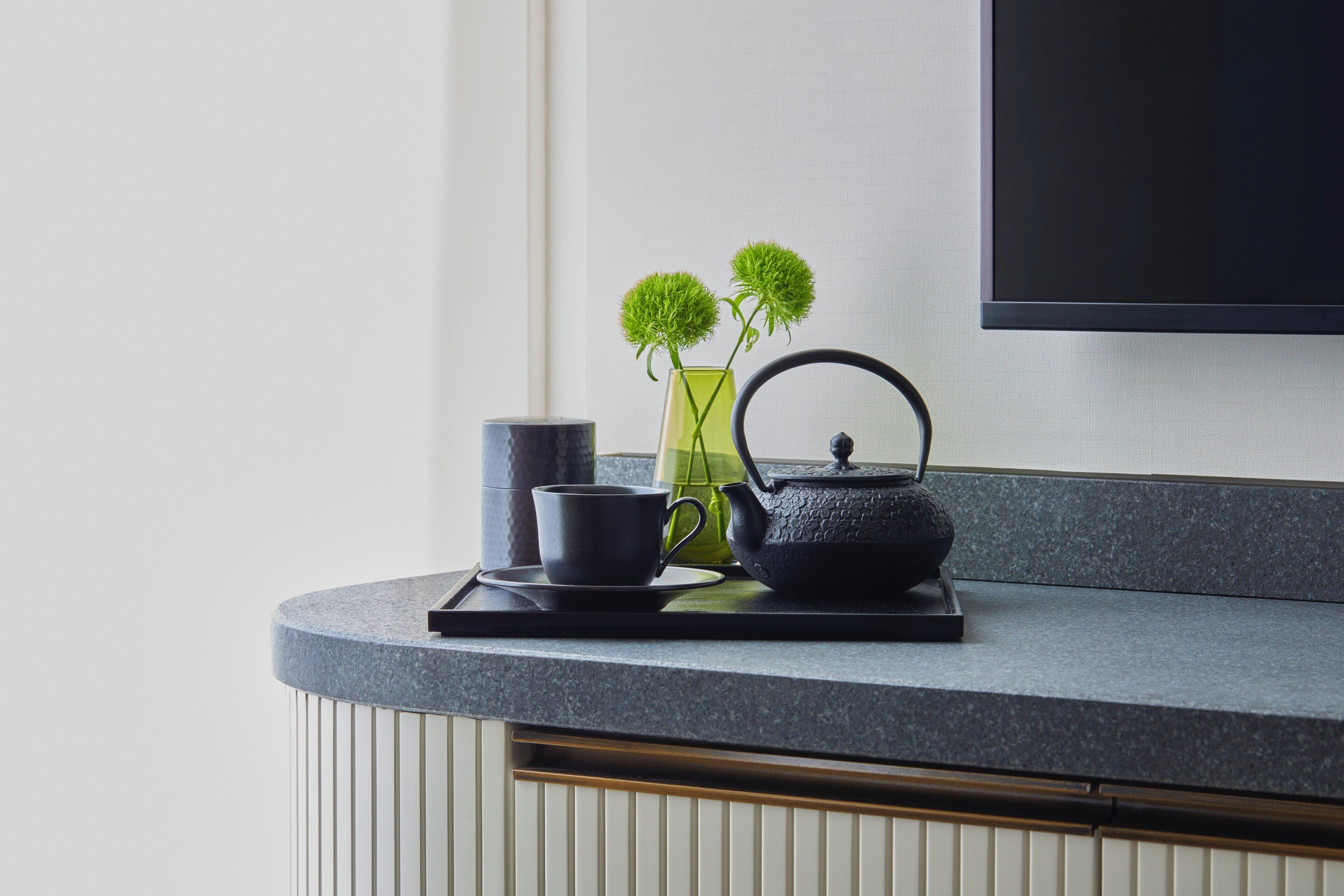Una encimera de cocina moderna con un juego de té, un jarrón verde con flores y un hervidor negro.