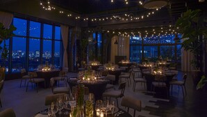 A spacious dining area with multiple tables set for a meal, large windows offering a city view, and string lights creating a warm ambiance. - Kimpton Shinjuku Tokyo by IHG (Tokyo)