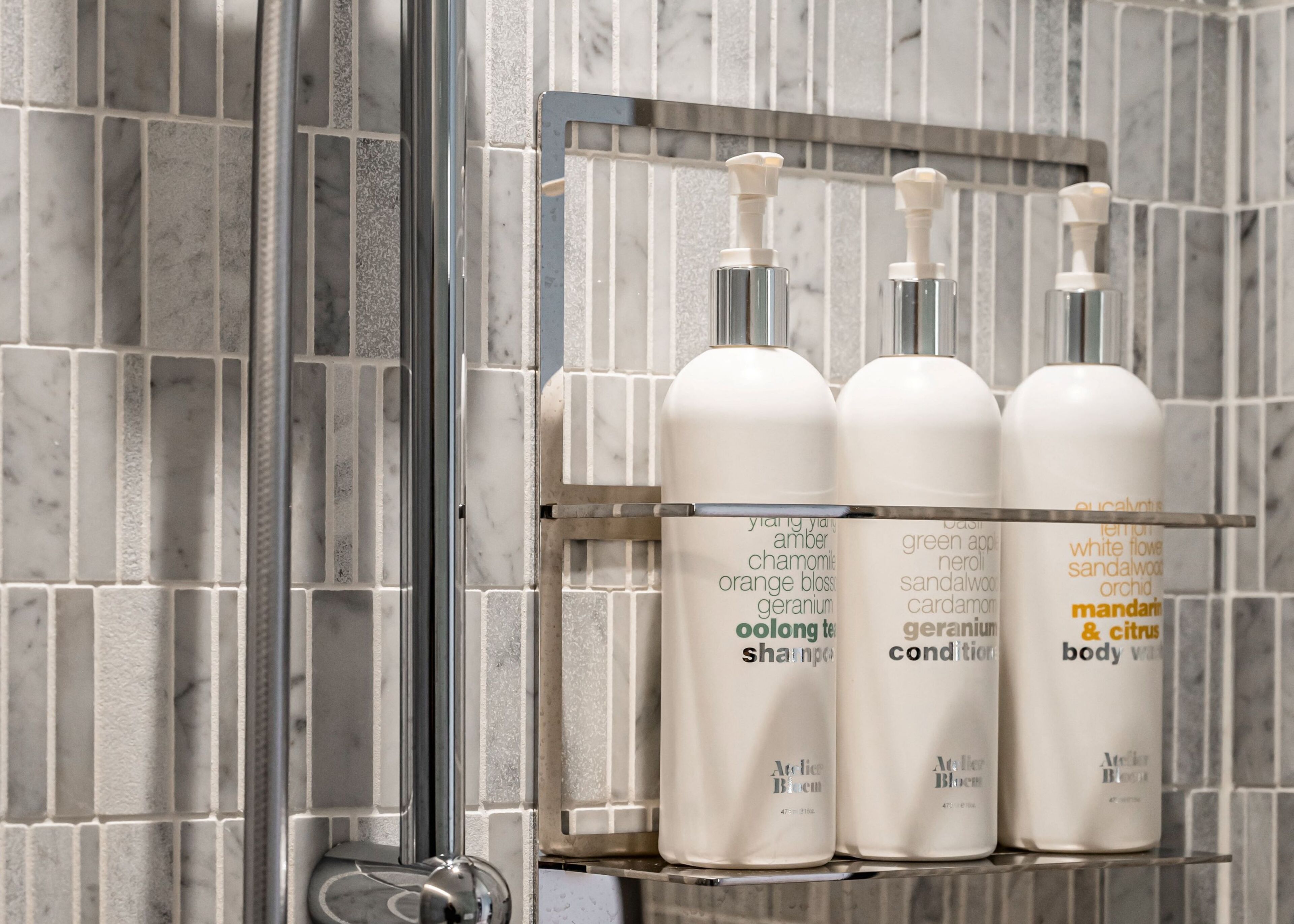 A bathroom with a tiled wall and a shelf holding three bottles of body wash.