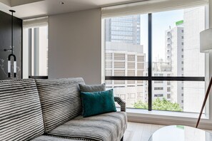 A modern living room with a striped sofa, a teal pillow, and a view of city buildings through large windows. - Kimpton Shinjuku Tokyo by IHG (Tokyo)