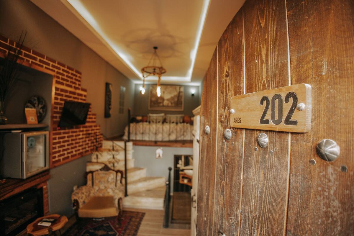 A wooden door with a number plate indicating room 202, a brick wall, a chandelier, and a staircase leading to another level.