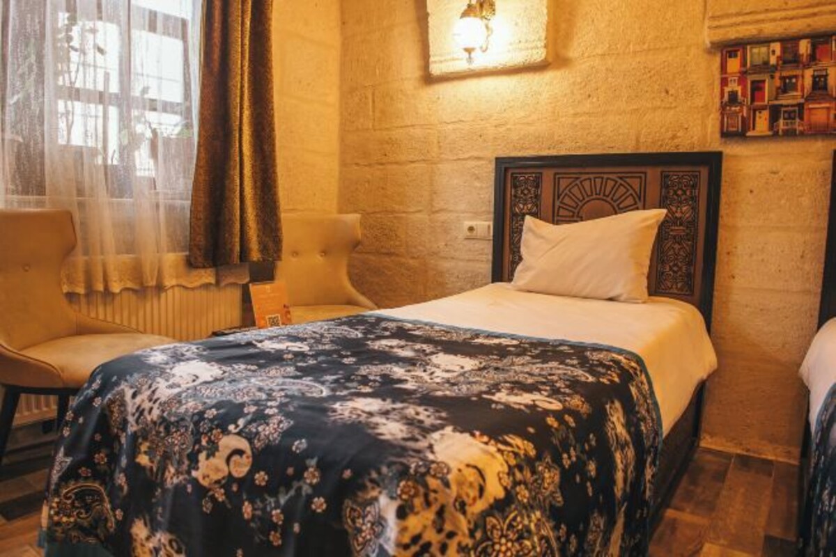 A hotel room with a bed, a chair, a window with curtains, and a wall with a textured finish.