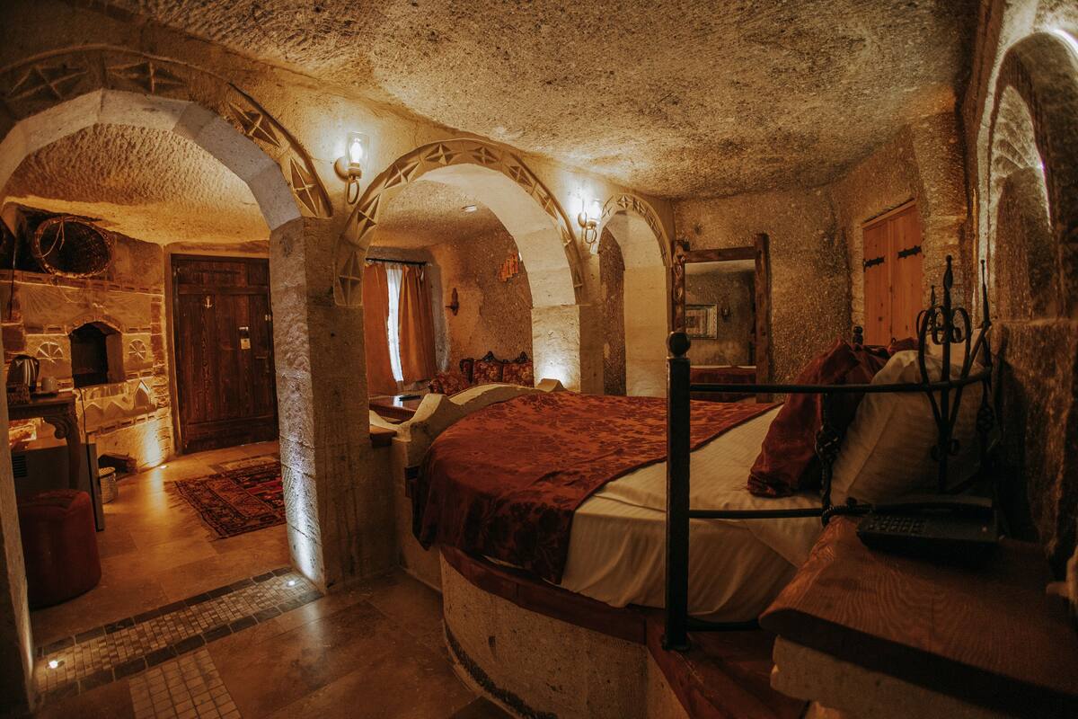 A stone-walled bedroom with a bed, a wooden wardrobe, and a stone bench.