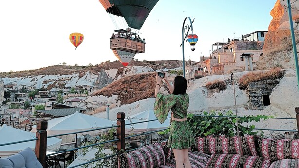 A hot air balloon with "CHINA SOUTHERN AIRLINES" written on it, a person taking a photo, and a view of a mountainous area with traditional buildings. - Vintage Cave House (Nevsehir)