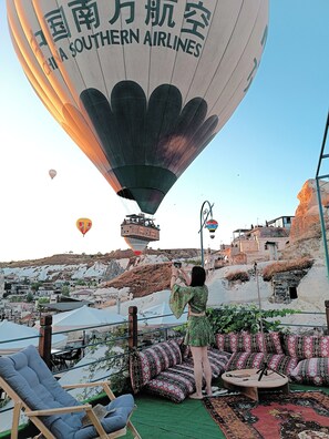 A hot air balloon with "CHINA SOUTHERN AIRLINES" written on it, a person taking a photo, and a view of a mountainous area with traditional buildings. - Vintage Cave House (Nevsehir)