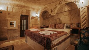 A stone-walled room with a bed, a wooden door, and a nightstand with a lamp. - Vintage Cave House (Nevsehir)