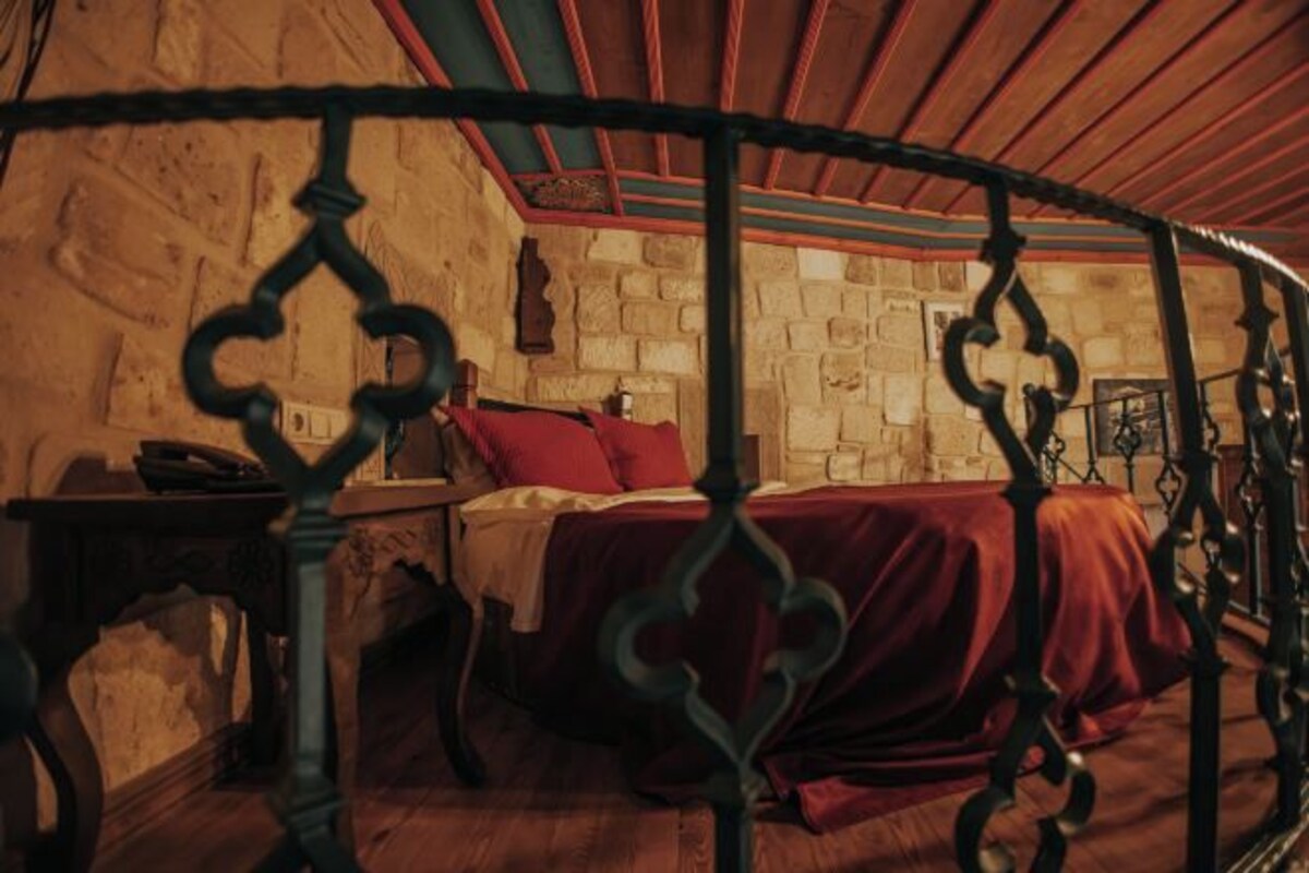 A room with a stone wall, a bed with a red bedspread, and a wooden ceiling.