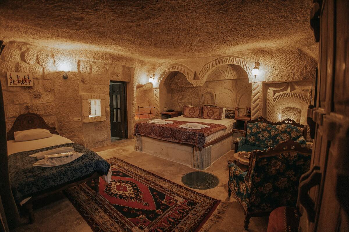 A room with a stone wall, a bed with a patterned bedspread, a chair with a floral design, and a rug with intricate patterns.