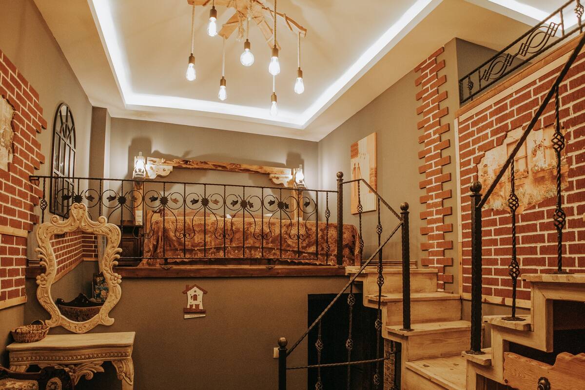 A staircase with a wooden finish and metal railings, leading to a loft area with a sloped ceiling and exposed brick walls.