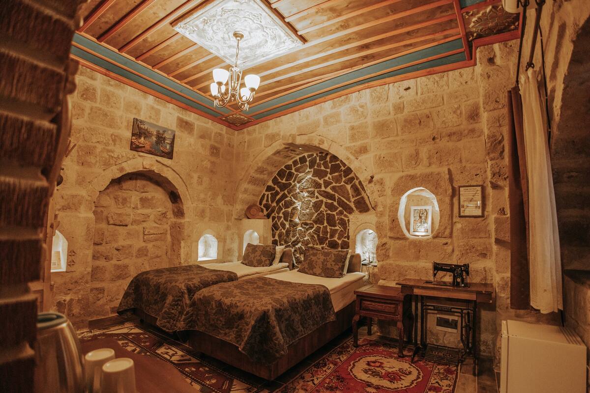 A room with stone walls, a large bed, a chandelier, and a vintage sewing machine.