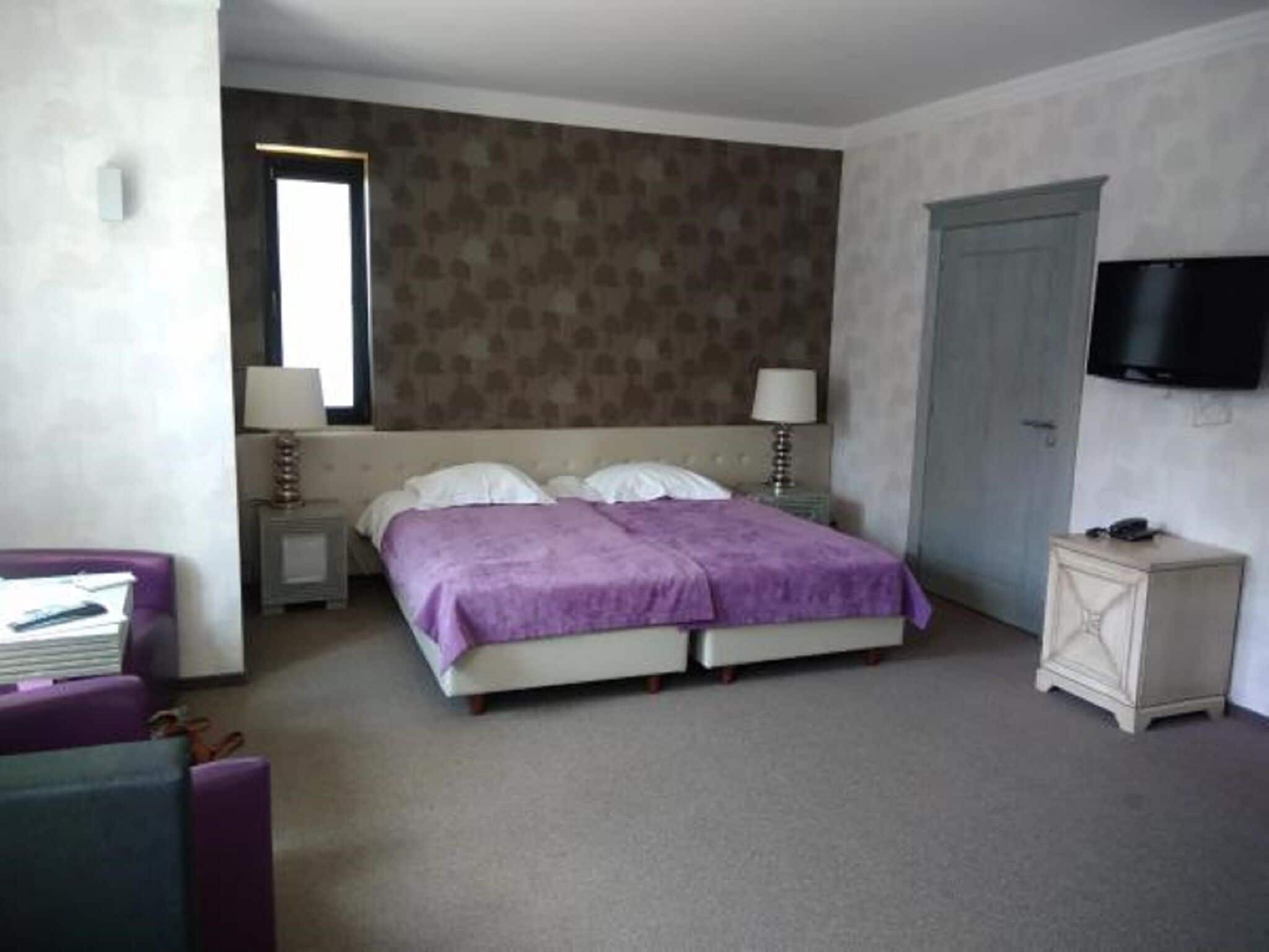 A bedroom with a bed, two bedside tables, a TV, a door, and a small cabinet.