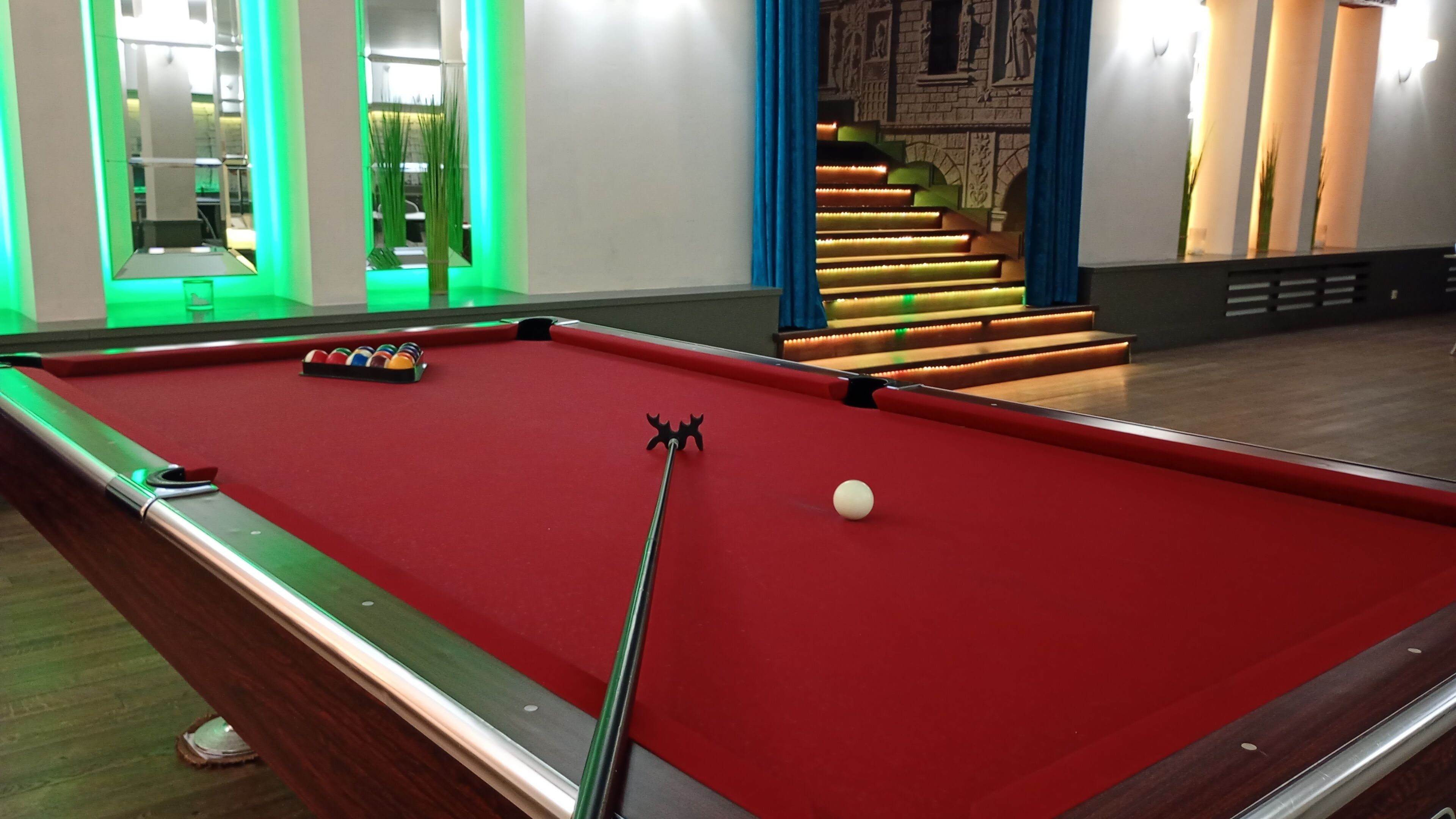 A pool table with a red felt surface, a cue stick, and a white cue ball.