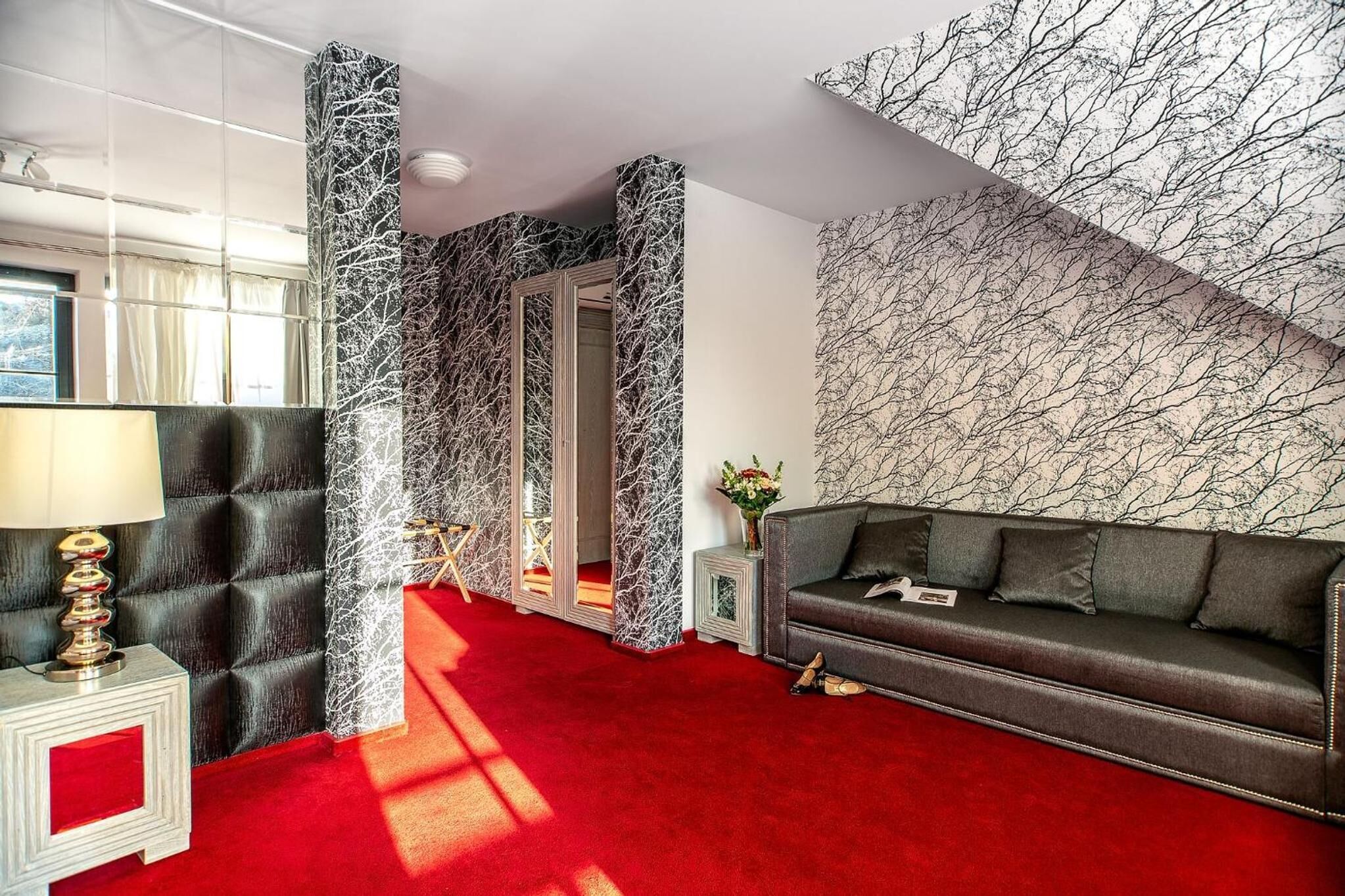 A room with a red carpet, a black leather sofa, a mirrored wall, and a patterned wall.